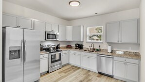 A modern kitchen with white cabinets, stainless steel appliances, a granite countertop, and a window with blinds. - 2BR Greer Condo: Pet-Friendly, King Beds, Fire Pit (Greer)