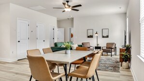 A modern dining area with a table and chairs, a ceiling fan, and a view into another room with a green sofa. - 2BR Greer Condo: Pet-Friendly, King Beds, Fire Pit (Greer)