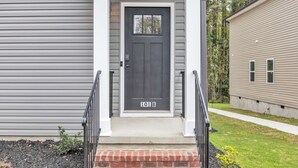 A gray house with a dark gray front door labeled "101 B" and a brick-paved front porch. - 2BR Greer Condo: Pet-Friendly, King Beds, Fire Pit (Greer)