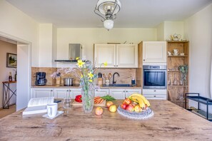 A modern kitchen with white cabinetry, a central island with fruits and flowers, and a coffee machine. - Vineyard Estate w/ Hot Tub Near Varaždin, Ludbreg, Croatia (Ludbreg)
