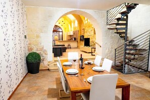 Un comedor con una mesa de madera dispuesta para cuatro, una escalera y una cocina al fondo.