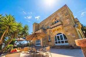 A stone building with a patio, outdoor furniture, and a large umbrella.
