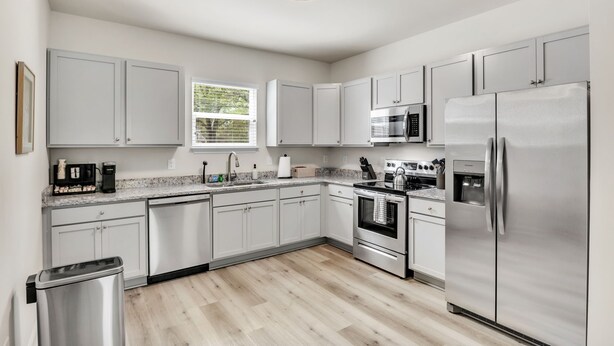 A modern kitchen with white cabinets, stainless steel appliances, and a window providing natural light. - Greer Charm: Pet-Friendly 2BR with Fire Pit (Greer)
