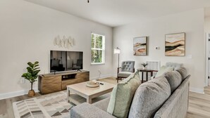 A modern living room with a flat-screen TV, a grey sofa, a wooden coffee table, and a patterned rug. - Greer Charm: Pet-Friendly 2BR with Fire Pit (Greer)