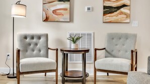 Two upholstered armchairs with wooden frames and a small round table with a plant, positioned in front of a wall-mounted air conditioning unit. - Greer Charm: Pet-Friendly 2BR with Fire Pit (Greer)