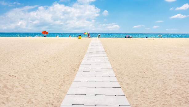 Una playa con cielo despejado, un camino pavimentado y sombrillas.