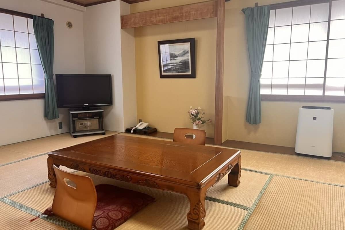 Ein traditioneller japanischer Raum mit Tatami-Böden, einem Holztisch, einem Fernseher und einer kleinen Klimaanlage.