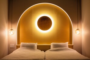 A hotel room with a bed, a circular light fixture above the headboard, and two pendant lights.