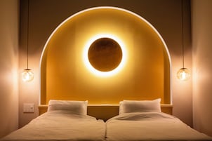 Una habitación de hotel con una cama, una lámpara circular sobre la cabecera y dos lámparas colgantes.