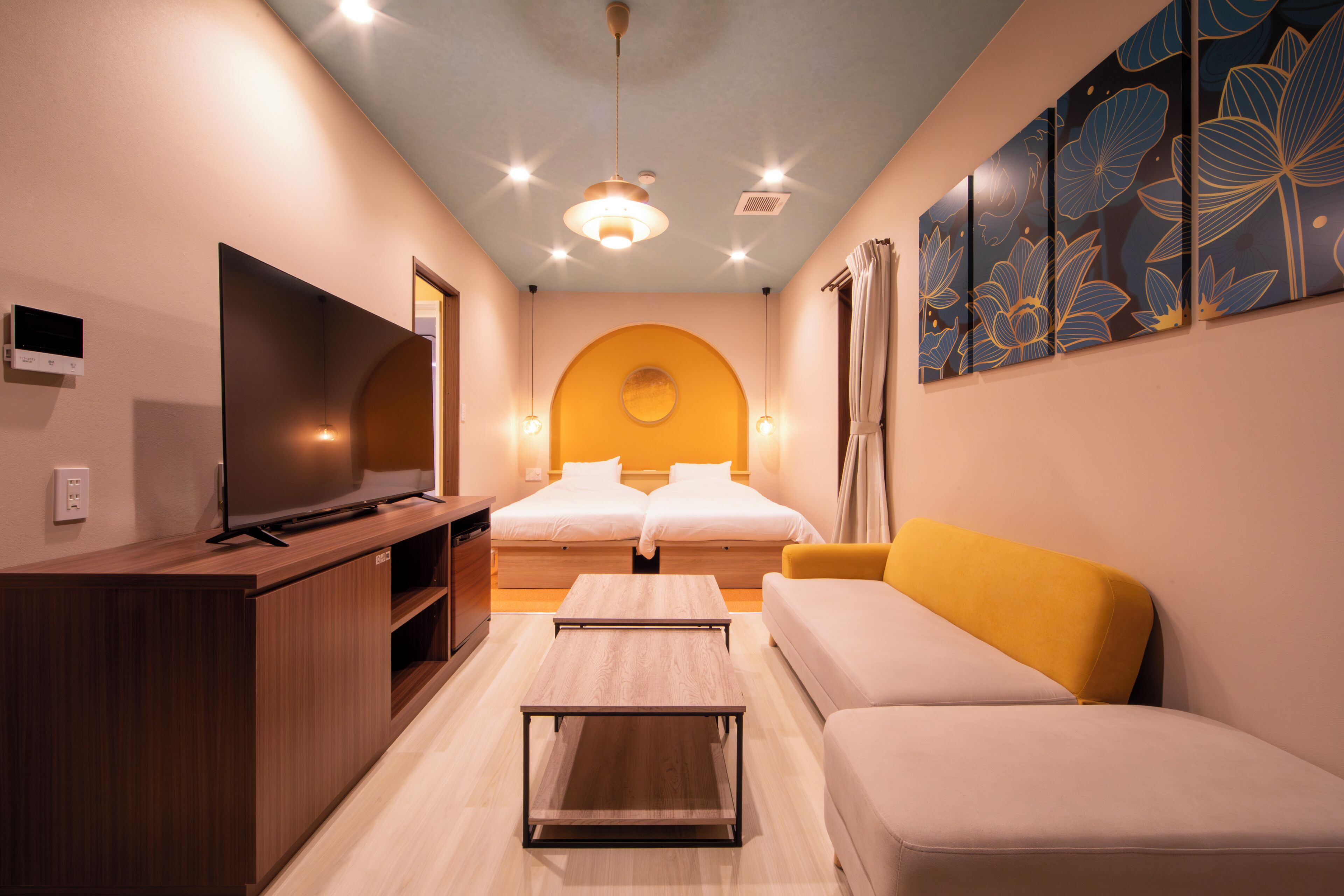 A hotel room with a TV, two beds, a sofa, a coffee table, and a wall with a floral design.