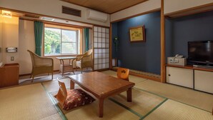 Ein traditioneller japanischer Raum mit Tatami-Böden, einem niedrigen Tisch, Stühlen, einem Fernseher und einem Fenster mit Blick auf Grünflächen.