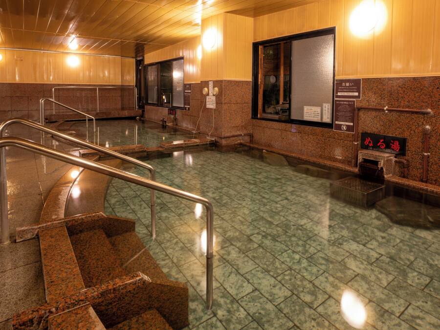 Un área de baños públicos con una escalera, barandillas de metal y piso de baldosas.
