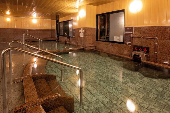 A public bath area with a staircase, metal handrails, and a tiled floor.