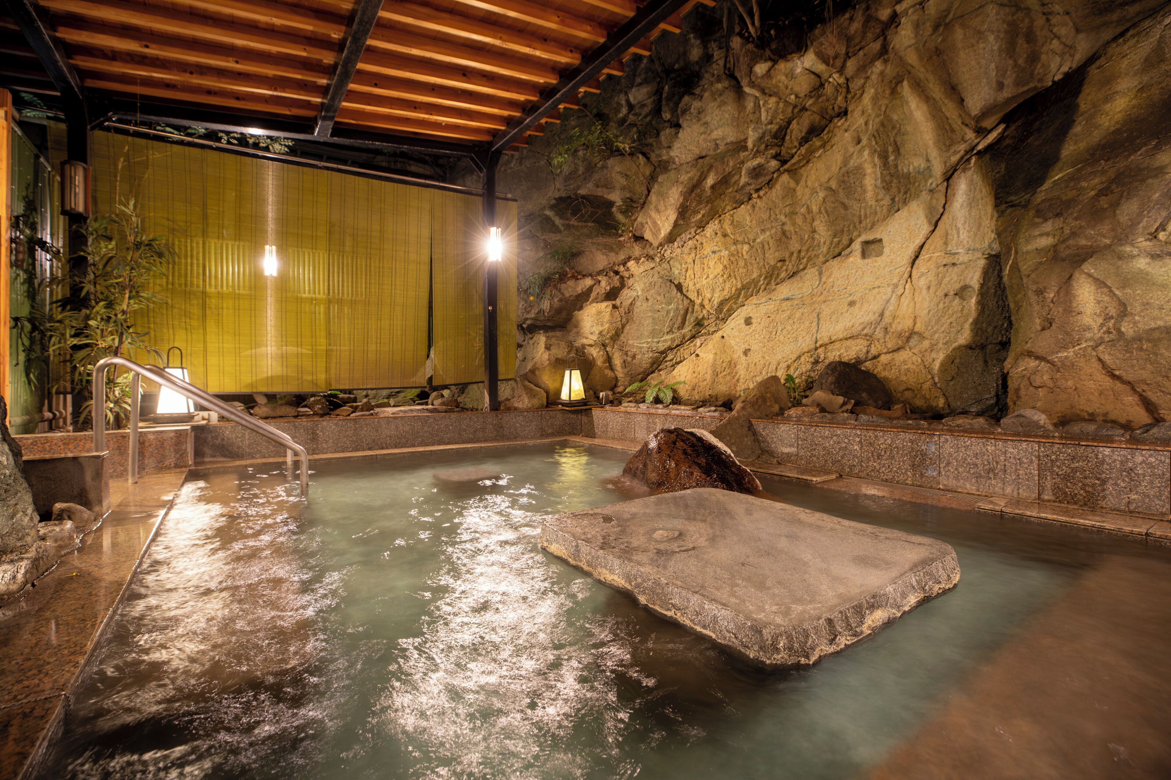 A hot spring bath with a wooden ceiling and a rocky wall.