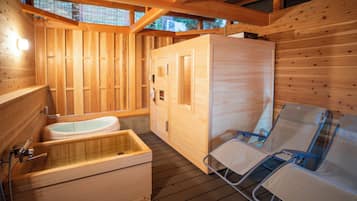 A wooden cabin with a wooden bathtub, a wooden sauna, and a reclining chair.