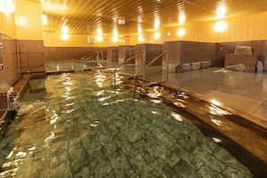 Piscina com água cristalina, rodeada por paredes de pedra e grades de metal.