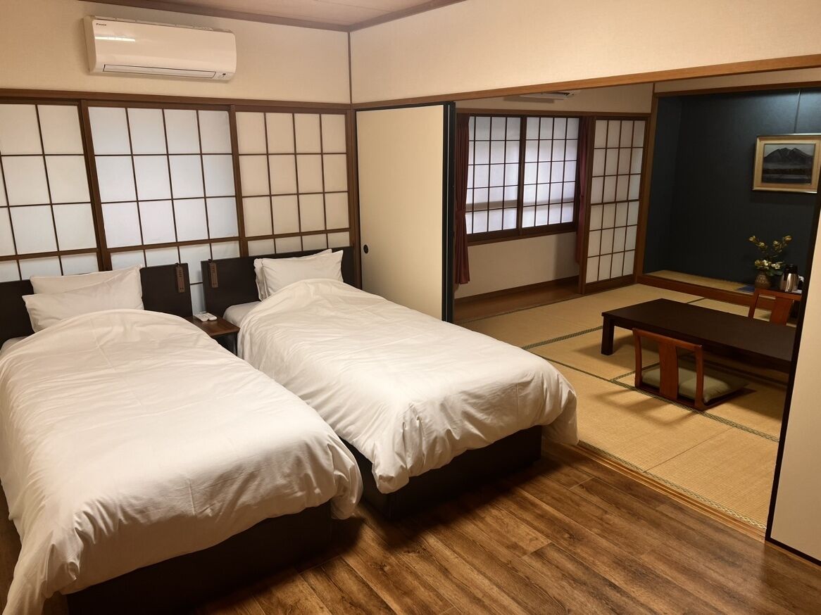 A room with two beds, a wooden floor, a sliding door, a small table, and a picture on the wall.
