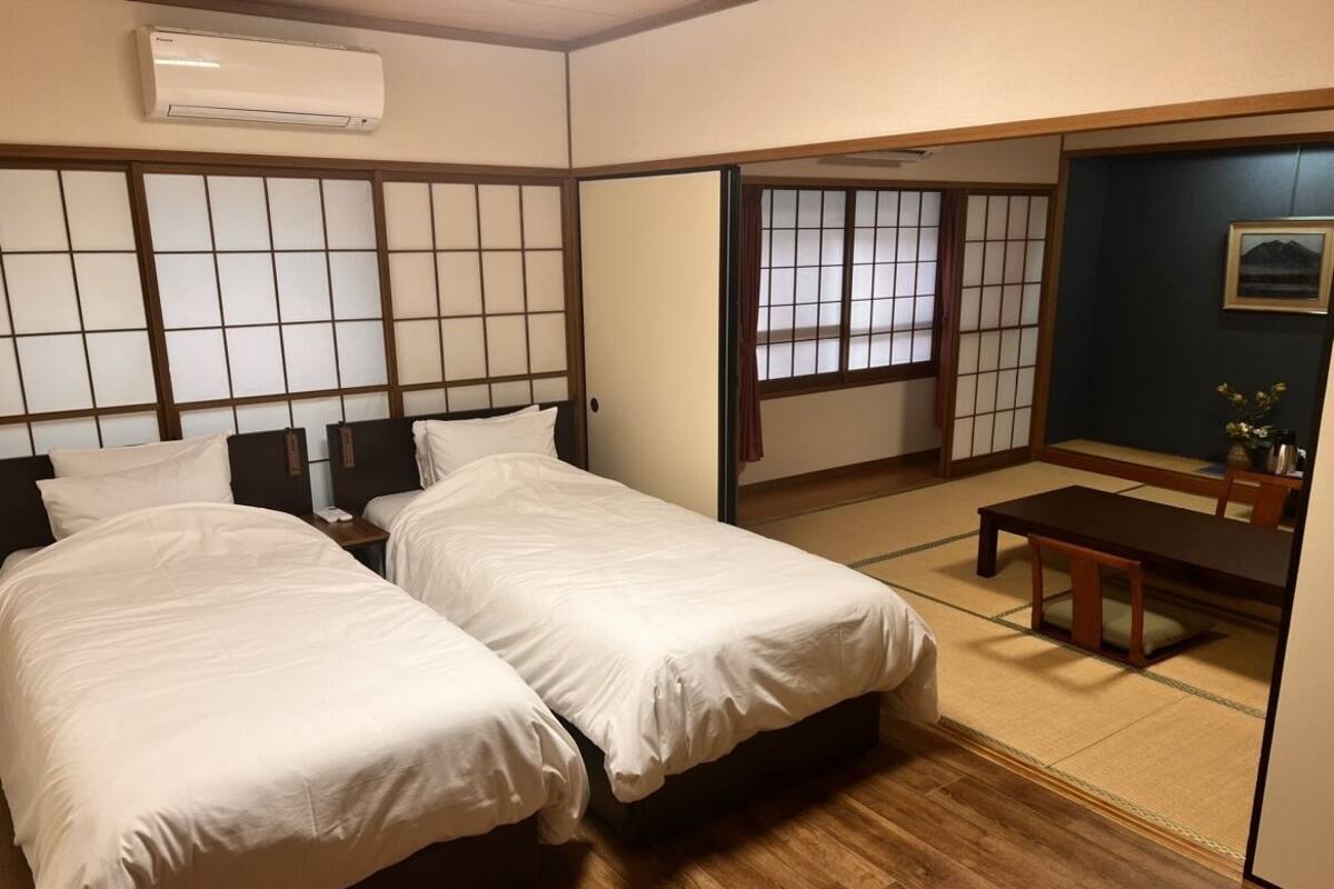 A room with two beds, a wooden floor, a sliding door, a small table, and a picture on the wall.