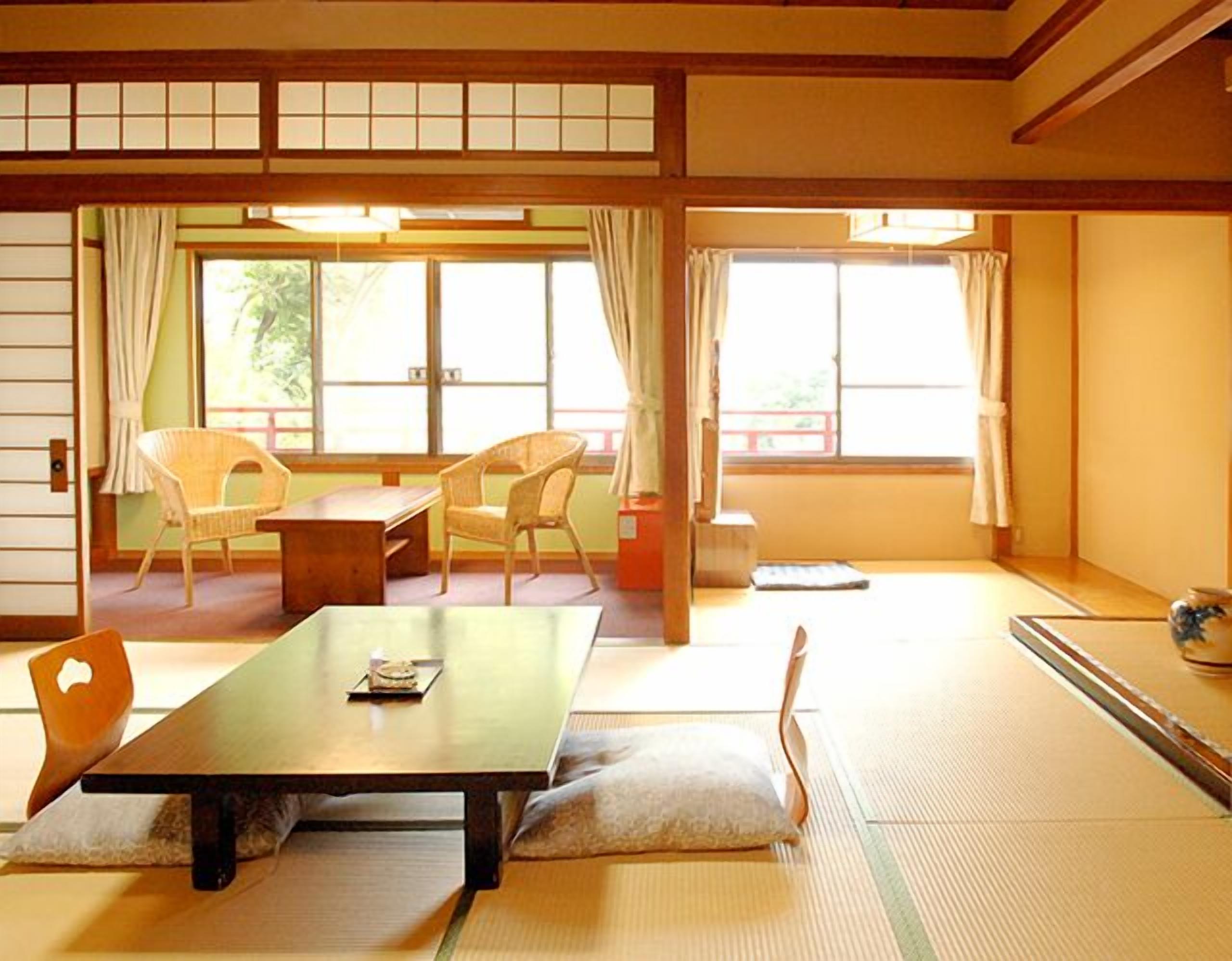 A traditional Japanese room with tatami flooring, a low table, two chairs, and sliding doors.