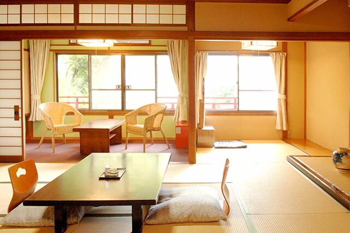 A traditional Japanese room with tatami flooring, a low table, two chairs, and sliding doors.