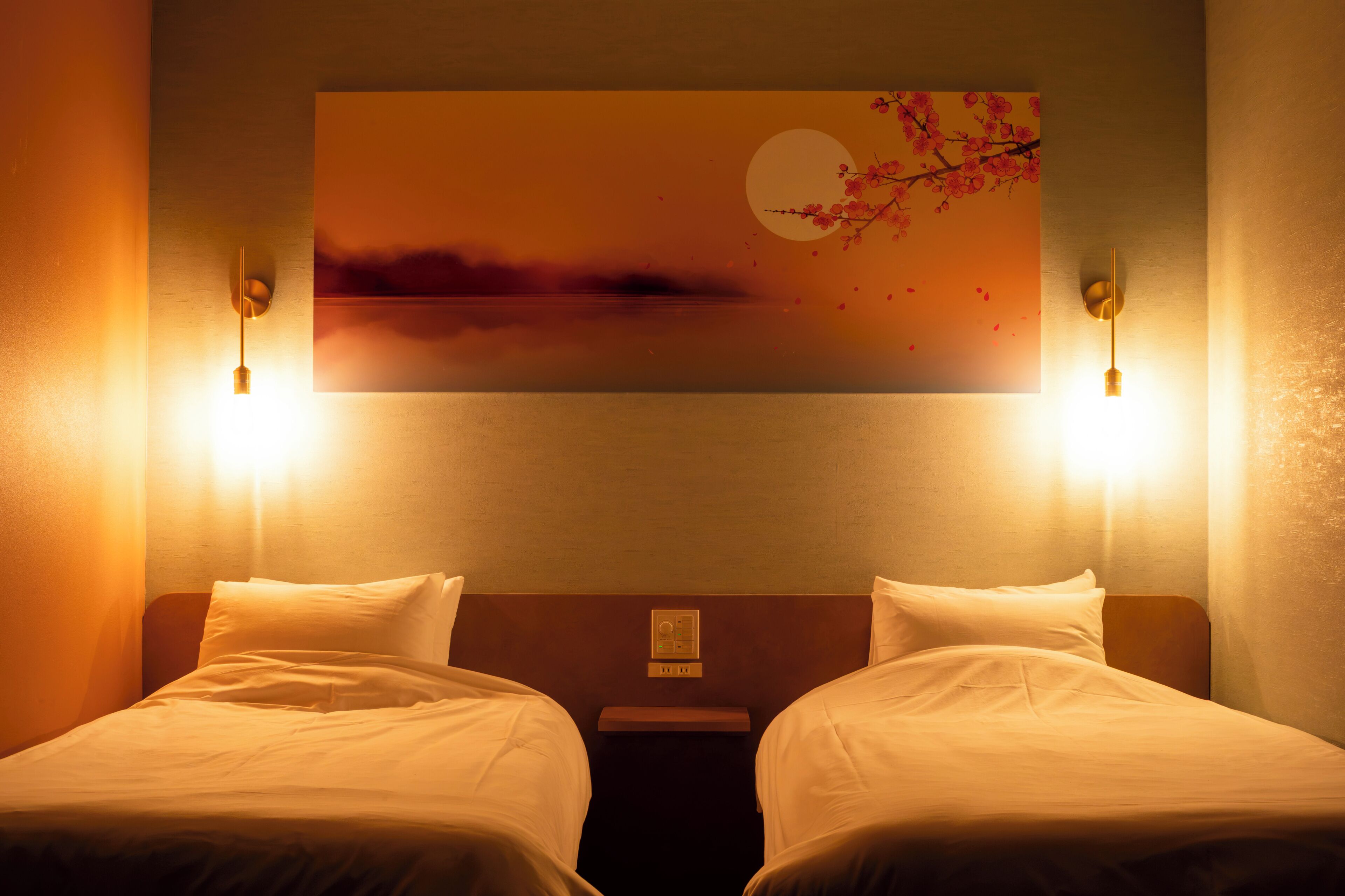 A hotel room with two beds, a nightstand, a wall-mounted artwork, and two wall-mounted lights.