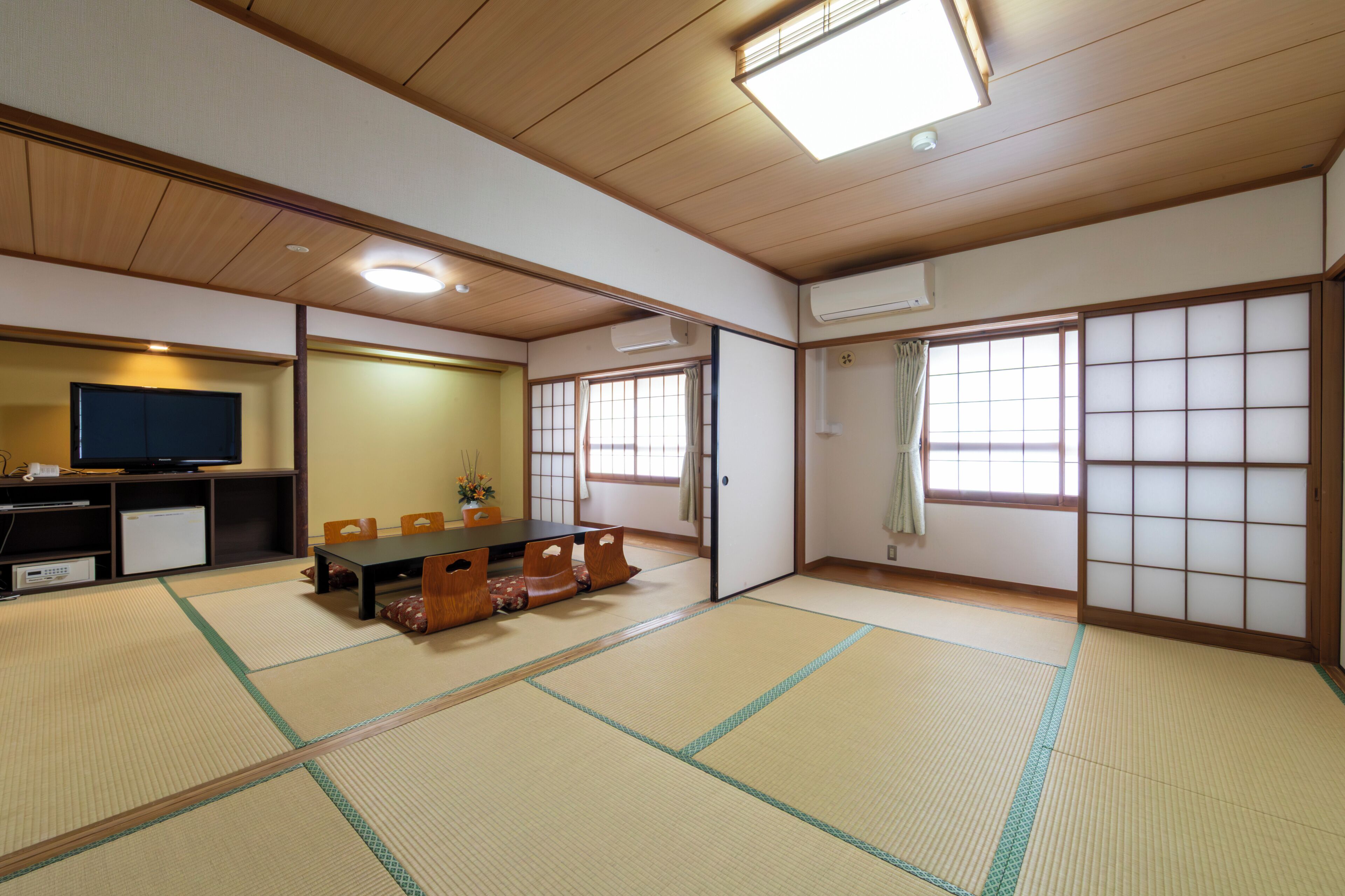 Una habitació tradicional japonesa amb terra de tatami, una taula baixa i coixins, una televisió i portes corredisses.
