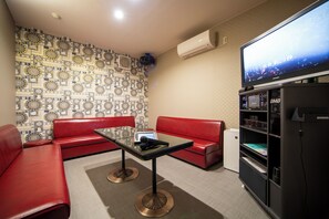 A hotel room with a red sofa, a glass table, a flat-screen TV, and a minibar.
