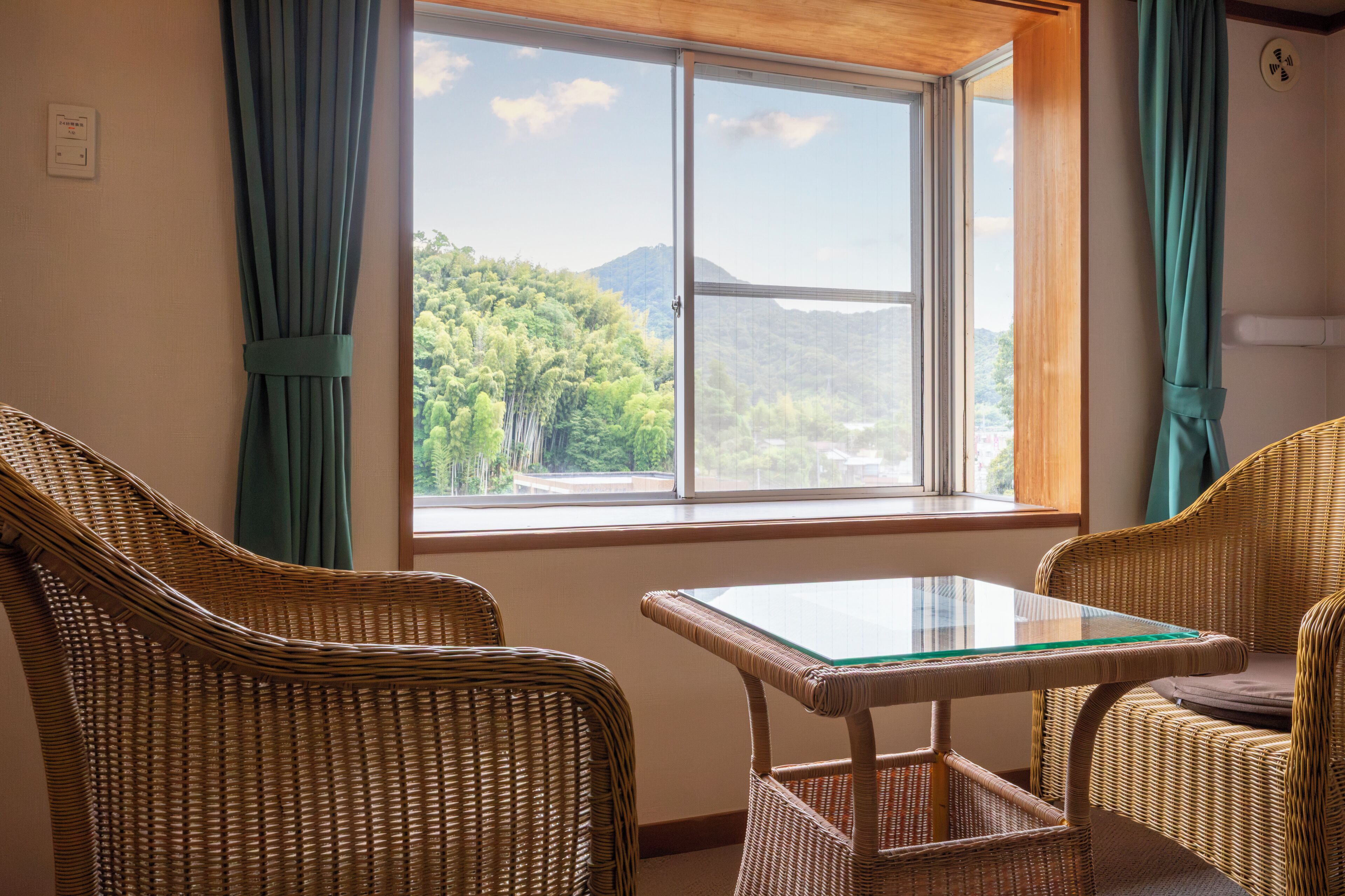 A room with a large window, wicker furniture, and a glass table.