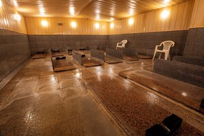 A sauna room with benches and chairs, wooden walls, and a tiled floor.