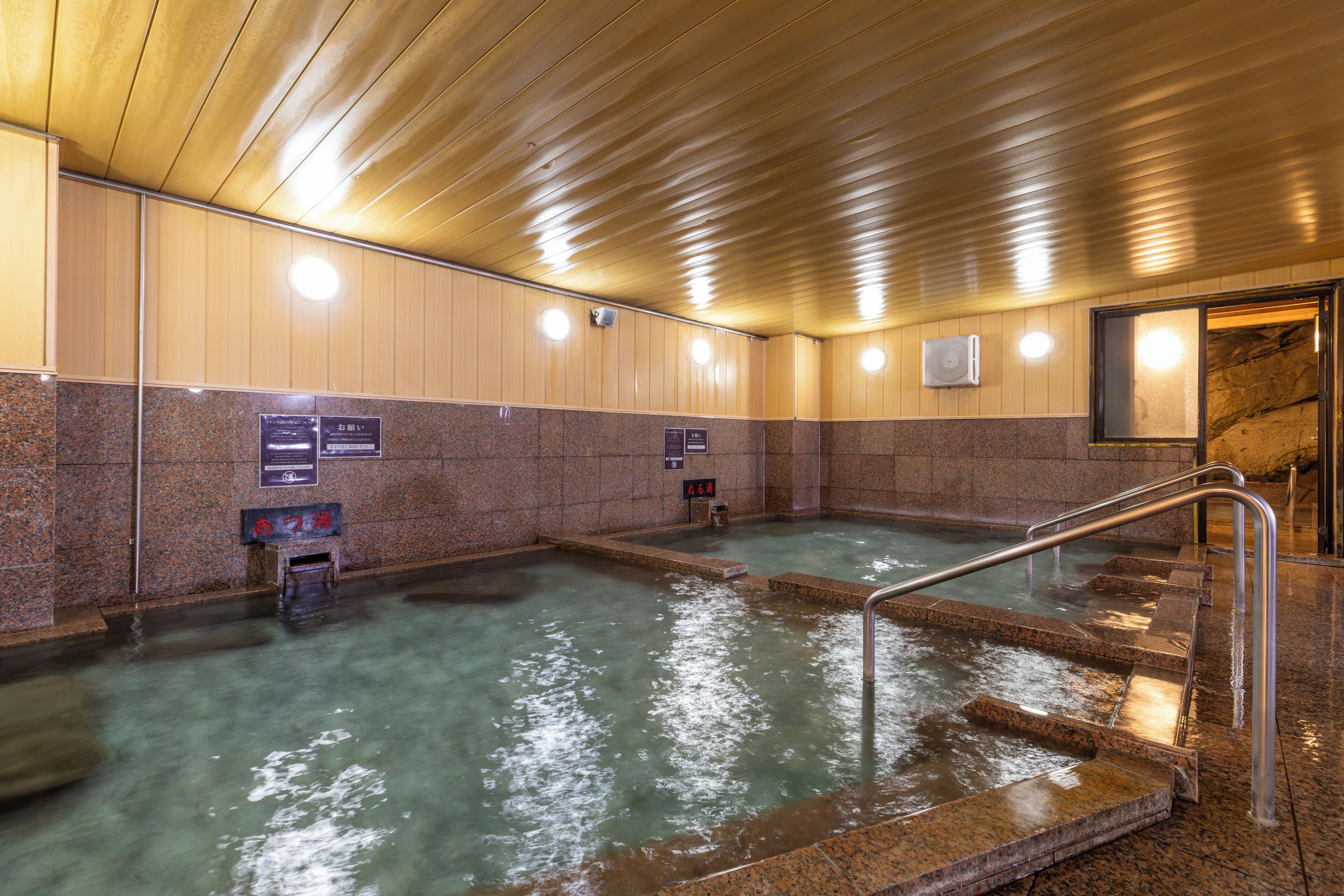 A hot spring bath area with tiled walls and a wooden ceiling.