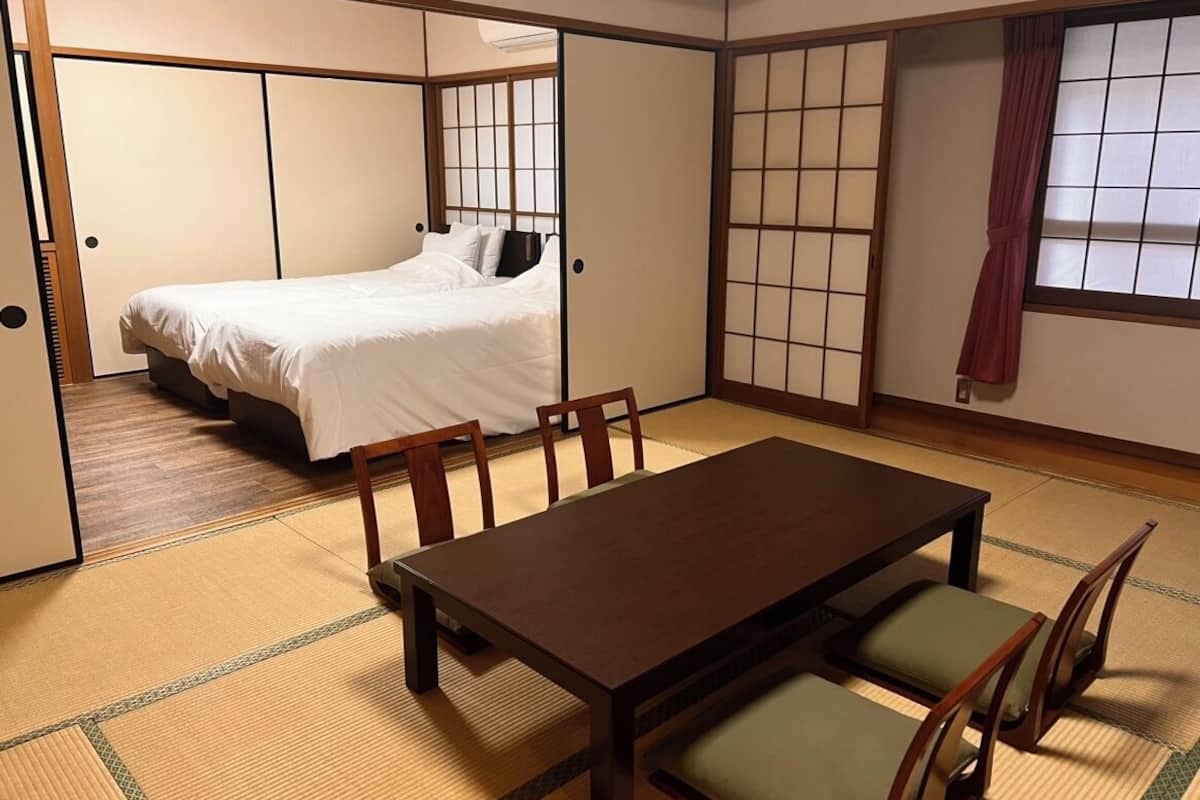 Ein traditioneller japanischer Raum mit Tatami-Boden, einem Bett, einem Esstisch mit Stühlen und verschiebbaren Shoji-Türen.