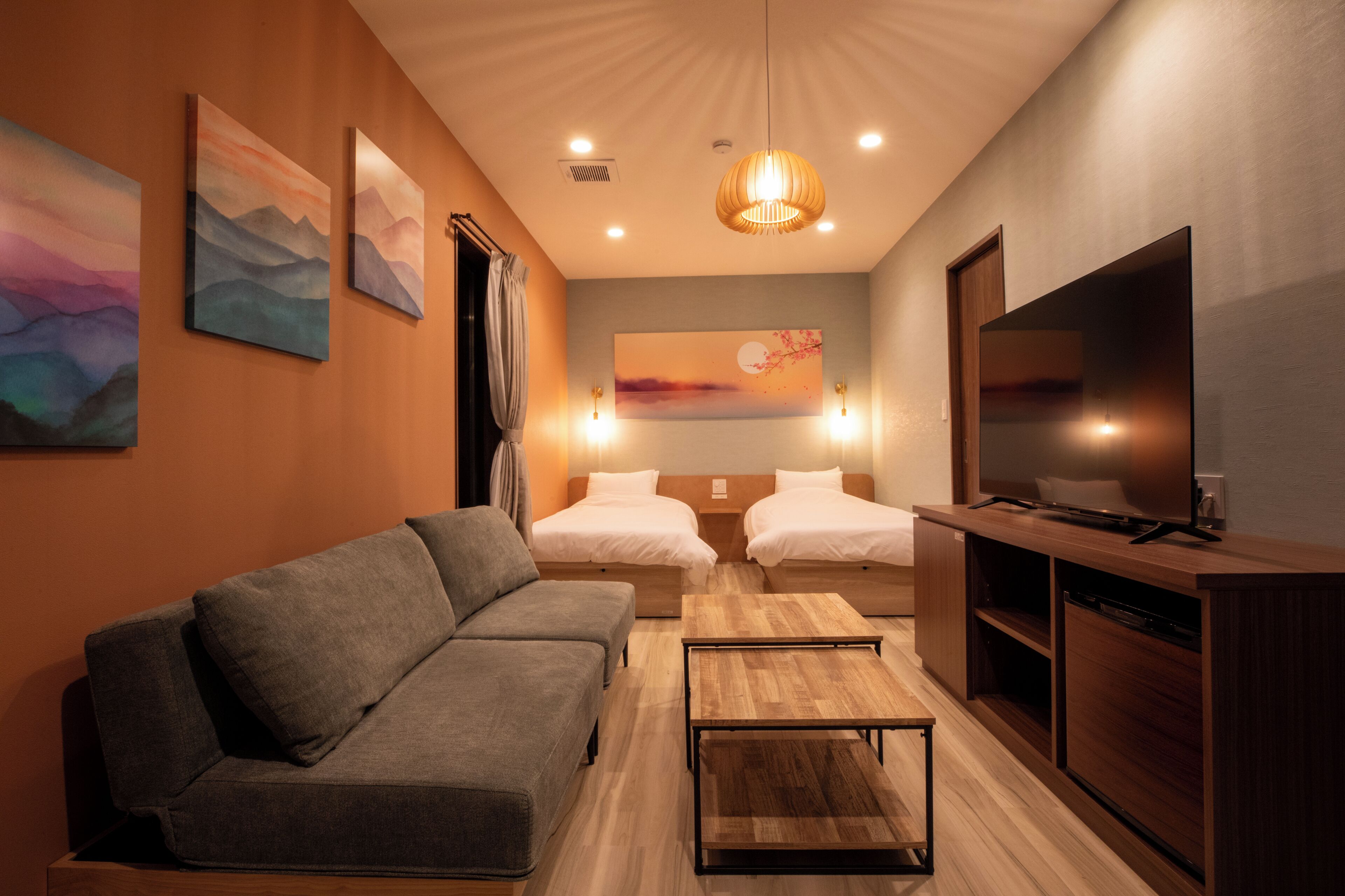 A modern hotel room with a sofa, two beds, a TV, artwork on the walls, and a wooden cabinet.