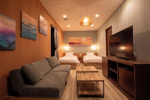 Quarto de hotel moderno com sofá, duas camas, televisão, obras de arte nas paredes e um armário de madeira.