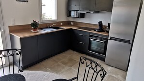 Eine moderne Küche mit integriertem Backofen, Mikrowelle und einem Edelstahl-Kühlschrank. Ein Spülbecken mit Armatur, ein Topf mit Pflanze und ein Fenster, das für natürliches Licht sorgt, sind ebenfalls vorhanden.
