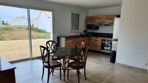A modern kitchen with wooden cabinets, a dining table with chairs, and a large window offering a view of the outdoors.
