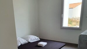 A small, sparsely furnished room with a single bed, a window, and a wooden floor.