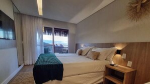 A bedroom with a large bed, a bedside table, a nightstand, a window with a view, and a balcony. - Pousada Divino Morro (Fernando de Noronha)