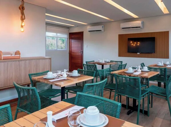 A dining area with multiple tables and chairs, air conditioning units, and a television mounted on the wall. - Pousada Divino Morro (Fernando de Noronha)