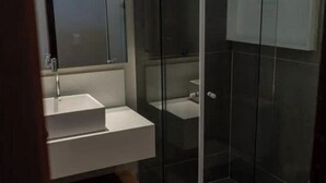 A modern bathroom with a glass shower enclosure, a white sink, and a toilet. - Pousada Divino Morro (Fernando de Noronha)