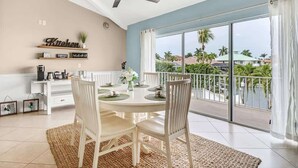 A dining area with a round table, white chairs, a ceiling fan, and a view of a balcony with palm trees. - 5BR Lush Marco Island Retreat (Marco Island)