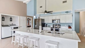 A modern kitchen with white cabinetry, a central island with bar stools, and a ceiling fan. - 5BR Lush Marco Island Retreat (Marco Island)