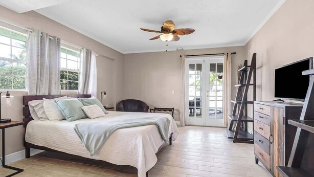 A bedroom with a bed, a TV, a ceiling fan, and a view of the outdoors. - 5BR Lush Marco Island Retreat (Marco Island)