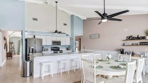 A modern kitchen with white cabinetry, a central island, and a dining area with white chairs and a round table. - 5BR Lush Marco Island Retreat (Marco Island)