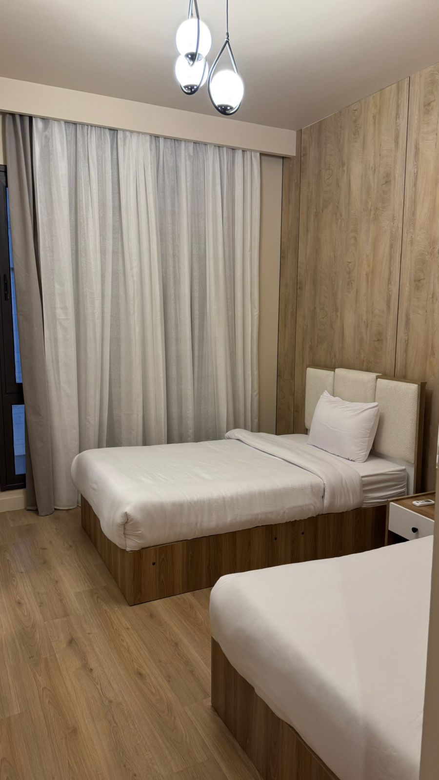 Un dormitorio moderno con dos camas, suelo de madera y un ventanal con cortinas.
