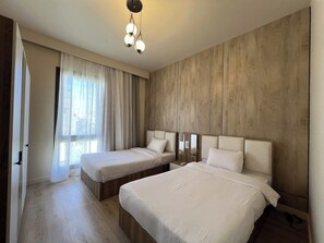 Camera d'albergo con due letti, parete in legno, una grande finestra con tende e un lampadario.