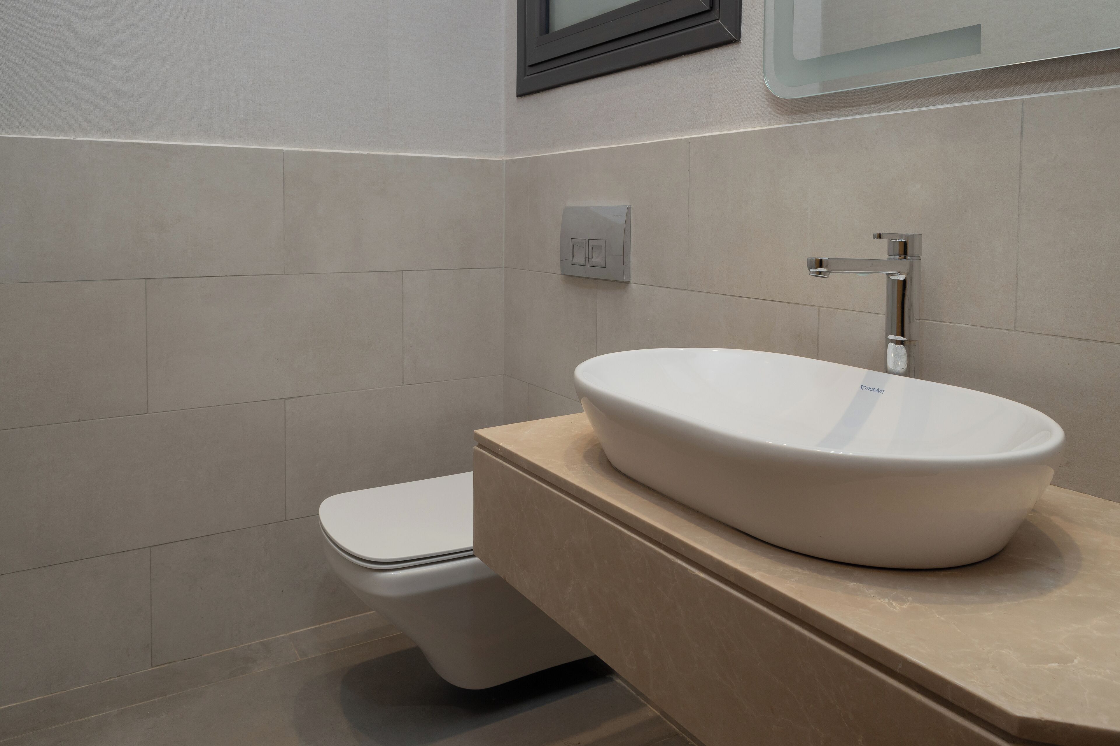 Ein modernes Badezimmer mit einer weißen Toilette, einem beige gefärbten Waschbecken und einem Spiegel darüber.