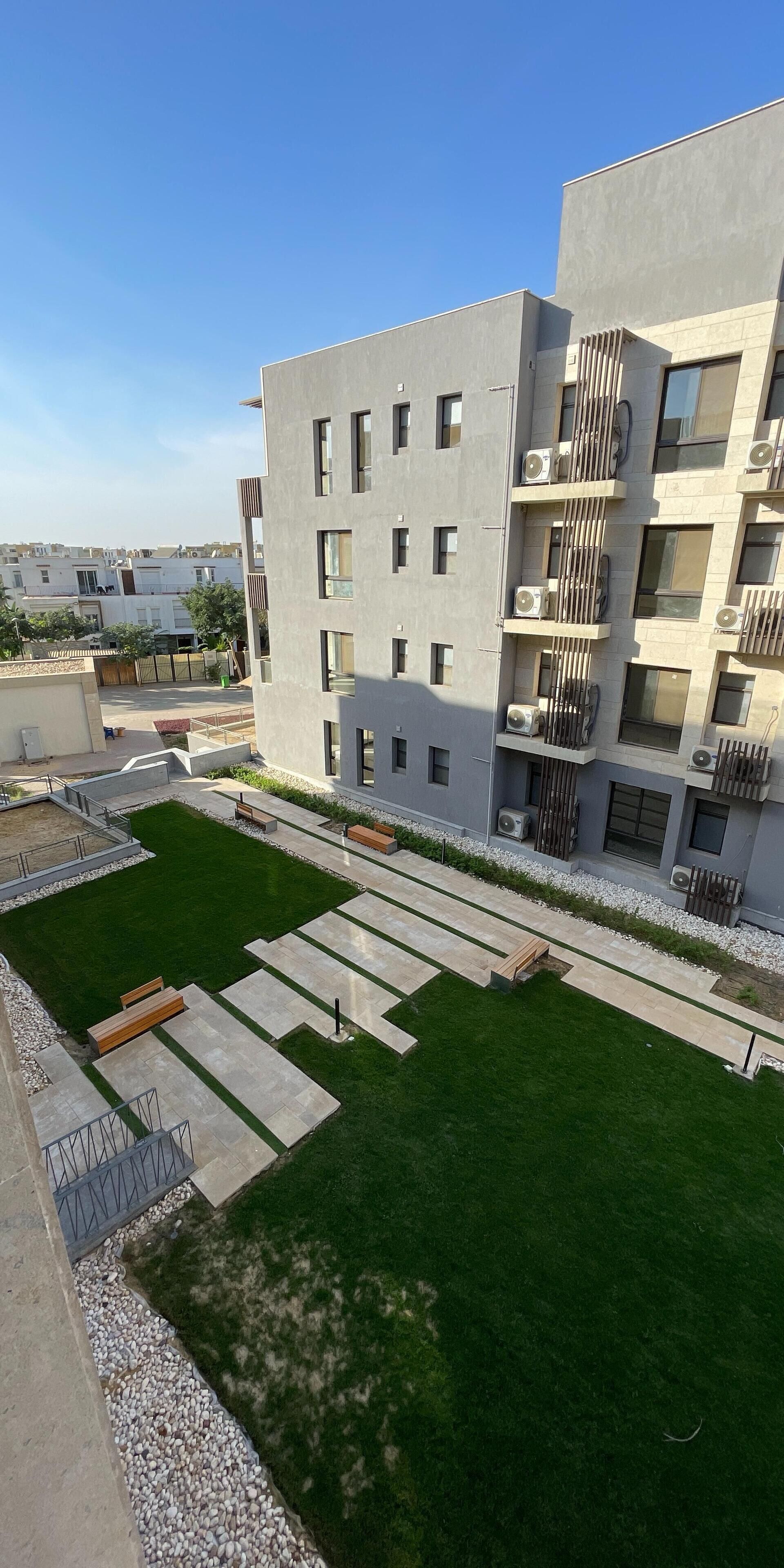 Un immeuble d’appartements moderne doté d’une cour intérieure comprenant une pelouse verdoyante, des espaces de détente et un chemin.