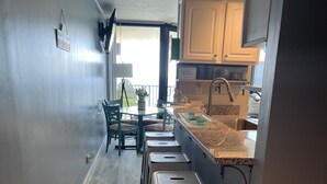 A kitchen with a wooden floor, a dining area with chairs, a kitchen island with stools, and cabinets. - Beachfront condo with amazing views of the sunset, family friendly, and safe. (Panama City Beach)