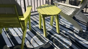 A balcony with yellow chairs and a table, overlooking a beach with a building in the background. - Beachfront condo with amazing views of the sunset, family friendly, and safe. (Panama City Beach)