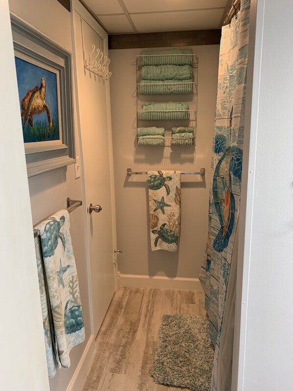 A bathroom with a wooden floor, a shower curtain with a sea turtle design, and a towel rack with multiple towels. - Beachfront condo with amazing views of the sunset, family friendly, and safe. (Panama City Beach)